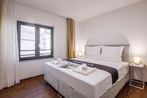 A hotel room with a bed, a window, a bedside table, and a lamp. - City Apartments (Rijeka)
