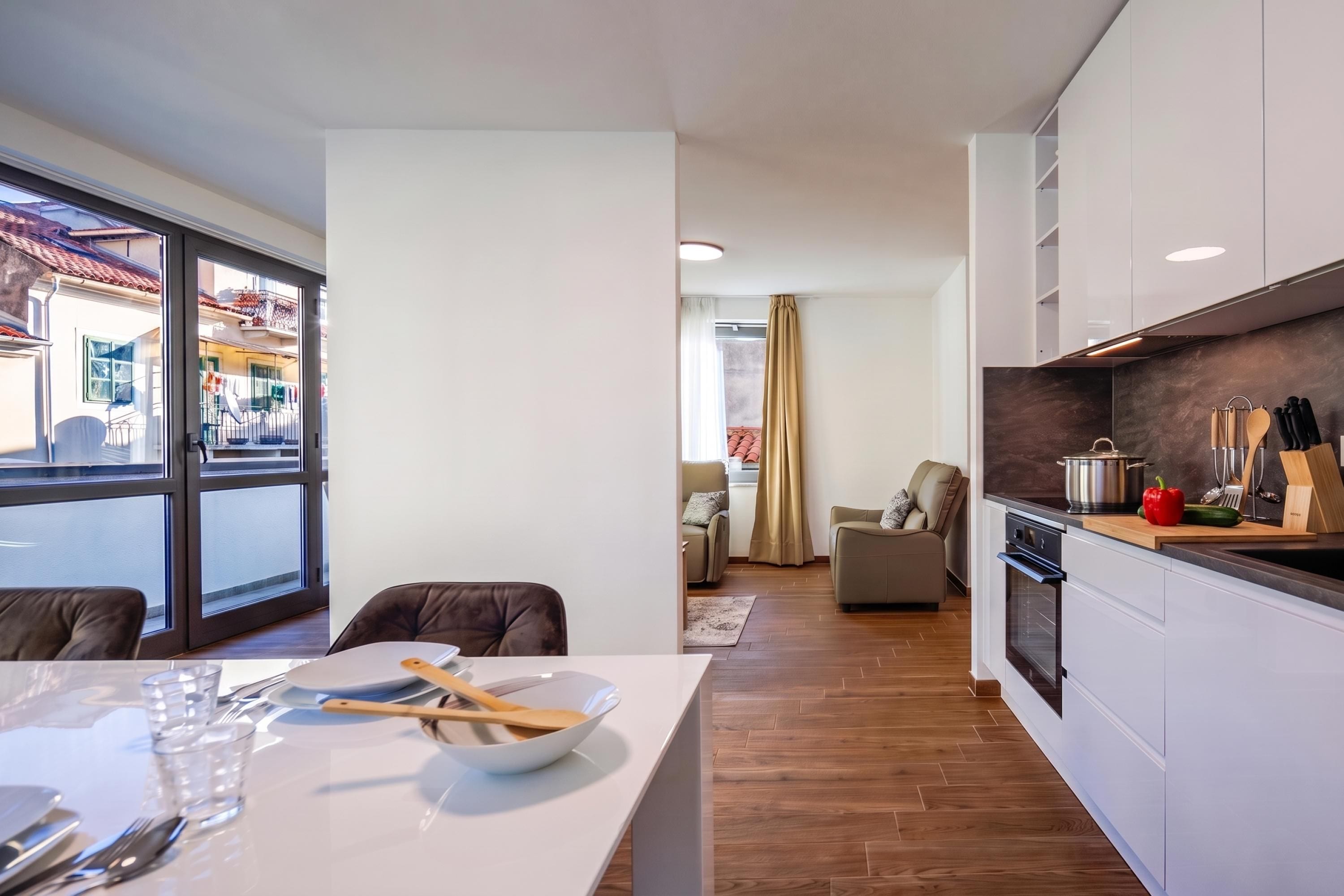 A modern kitchen with a dining area, wooden flooring, and a view of the street outside.