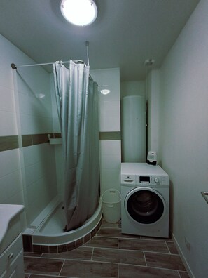 Pieni kylpyhuone, jossa on suihku, pesukone ja wc.