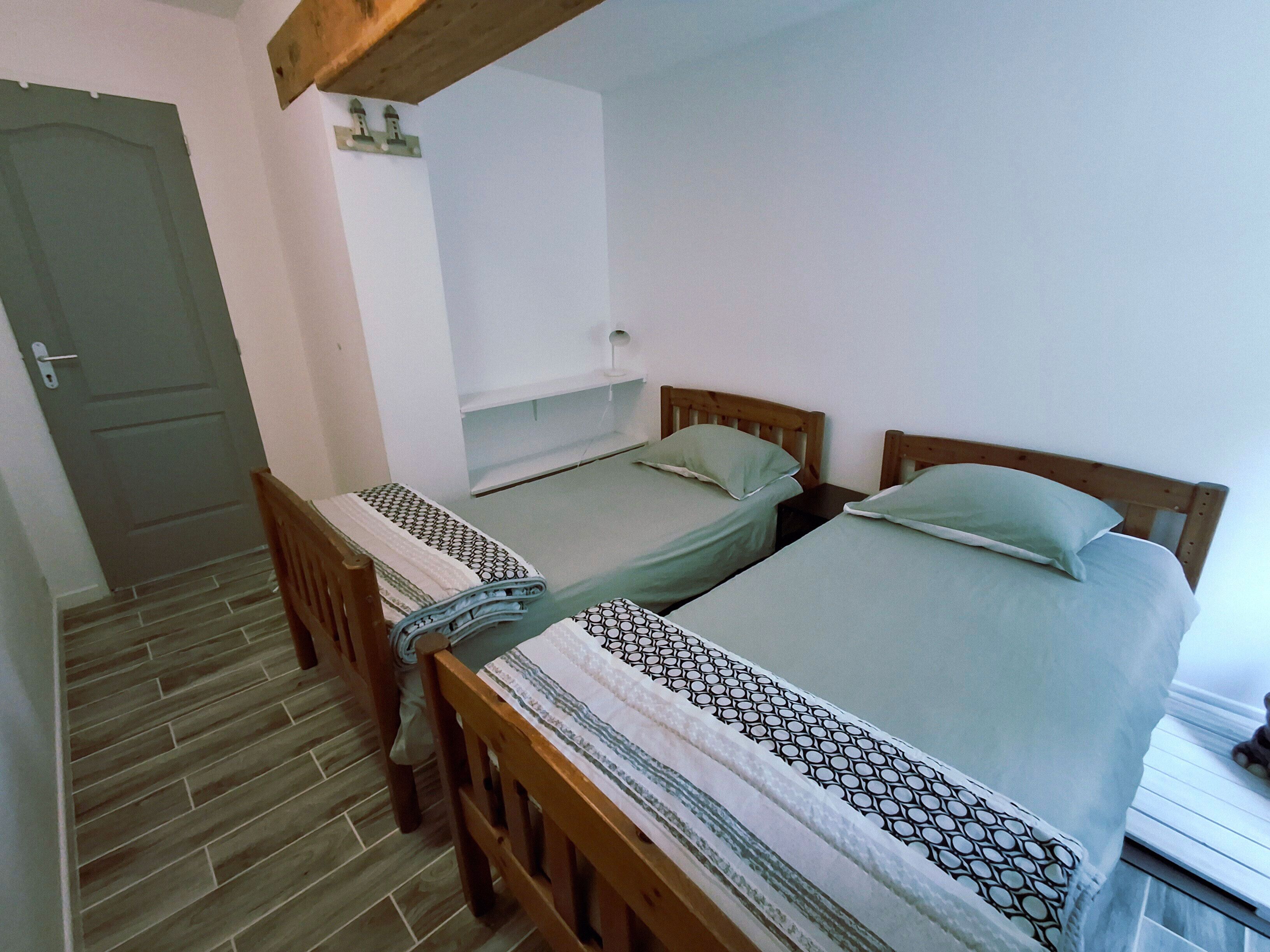 A room with two wooden beds, a wooden chair, a small table, and a door.