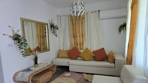 A living room with a white sofa, a wooden side table, a mirror, and a ceiling light fixture. - DUERMES CON LA NATURALEZA (Ramos)