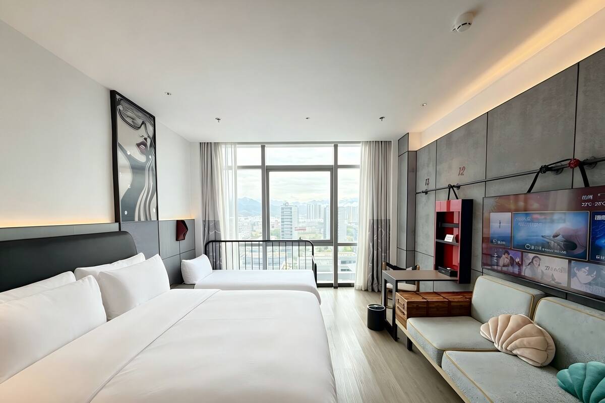 Habitación de hotel con dos camas, un sofá, televisión y un ventanal con vistas a la ciudad.