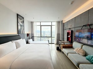 Ett hotellrum med två sängar, en soffa, en TV och ett stort fönster med utsikt över staden.