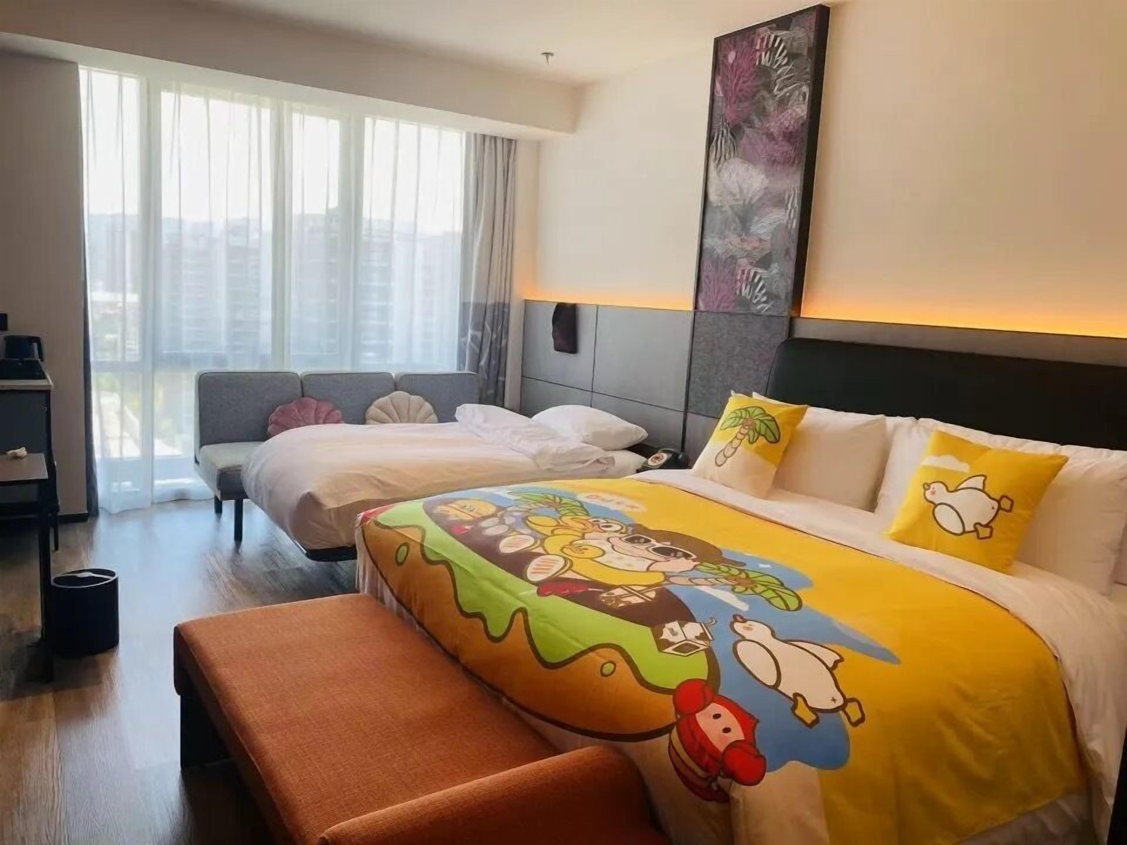 Habitación de hotel con una cama grande, una cama más pequeña, un banco y vistas a la ciudad a través de amplias ventanas.