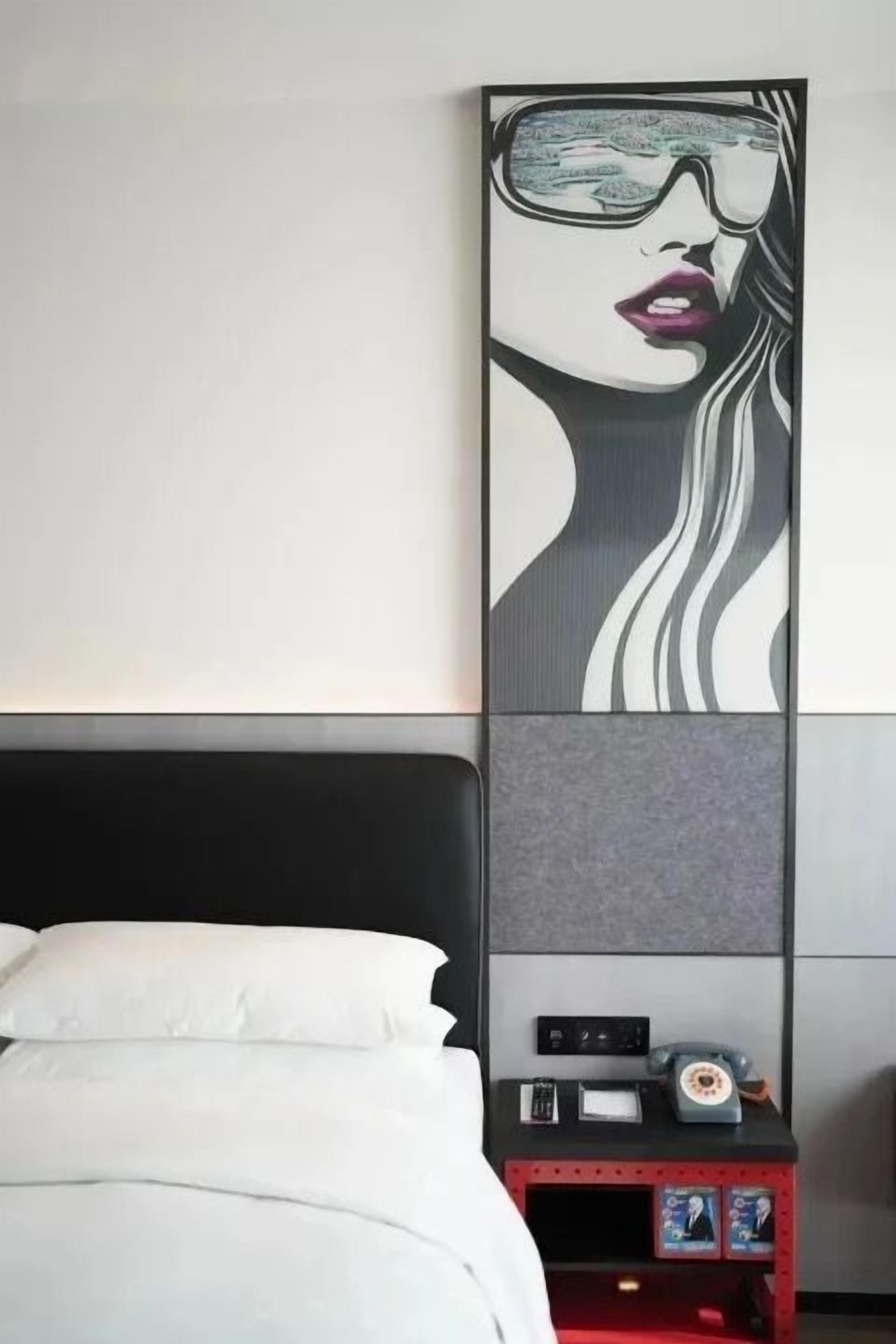 Habitación de hotel con cama, mesita de noche con un reloj y una obra de arte colgada en la pared.