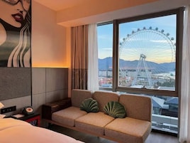Habitación de hotel con un ventanal grande, un sofá con almohadones decorativos, una cama y una obra de arte colgada en la pared.