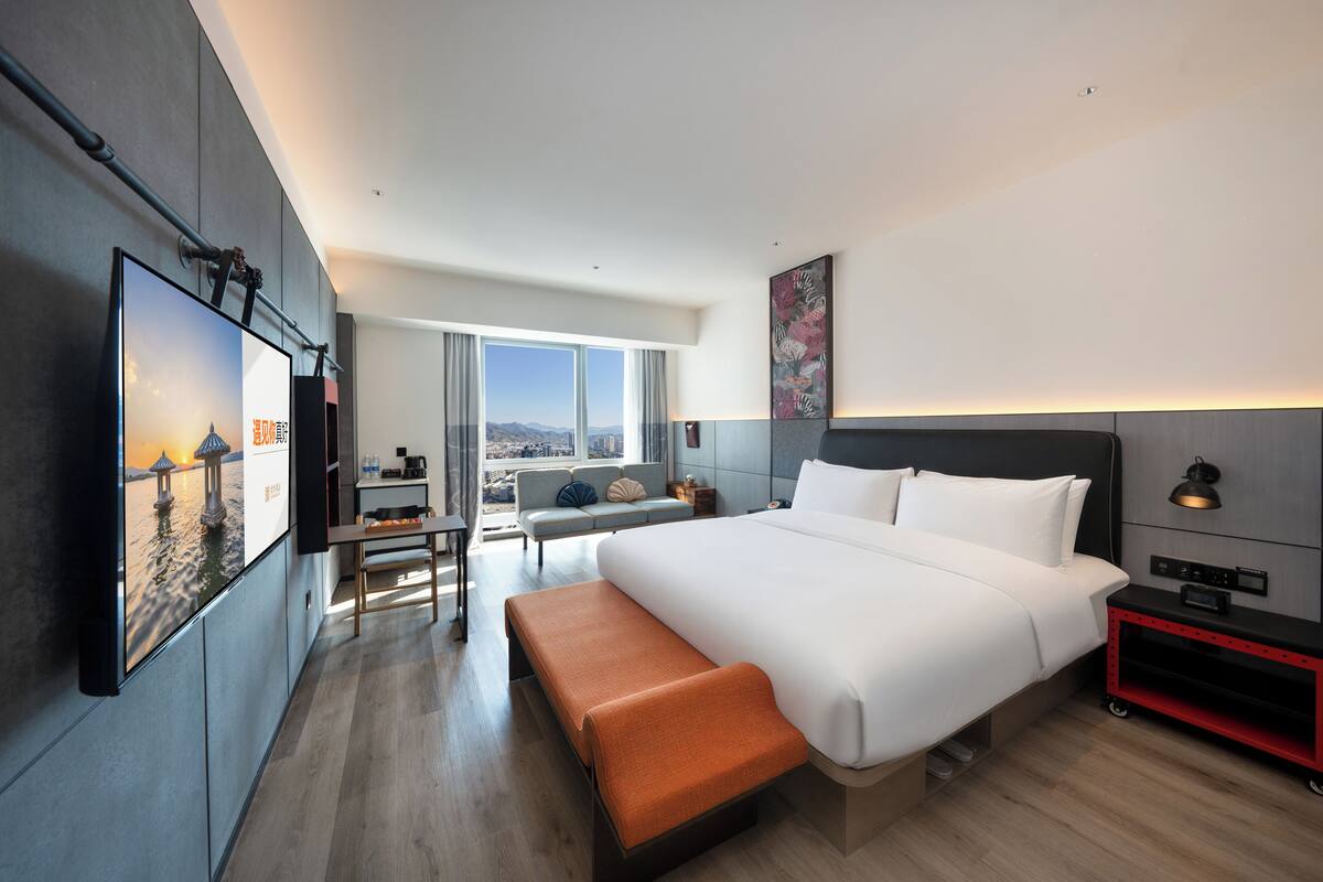 Una habitación de hotel moderna con una cama grande, una banca, un escritorio y vistas a la ciudad.