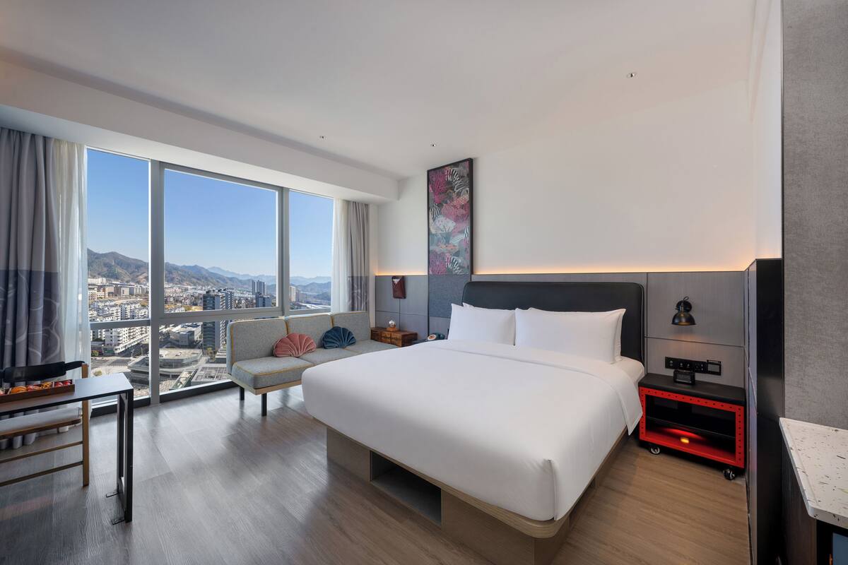 Una habitación de hotel moderna con una cama grande, un escritorio, una silla y vistas a la ciudad.