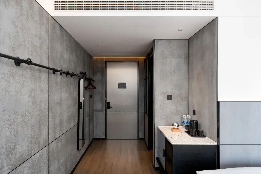 A narrow hallway with a door at the end, a towel rack on the left, and a small kitchenette area on the right.