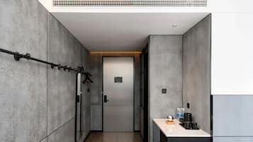 A narrow hallway with a door at the end, a towel rack on the left, and a small kitchenette area on the right.