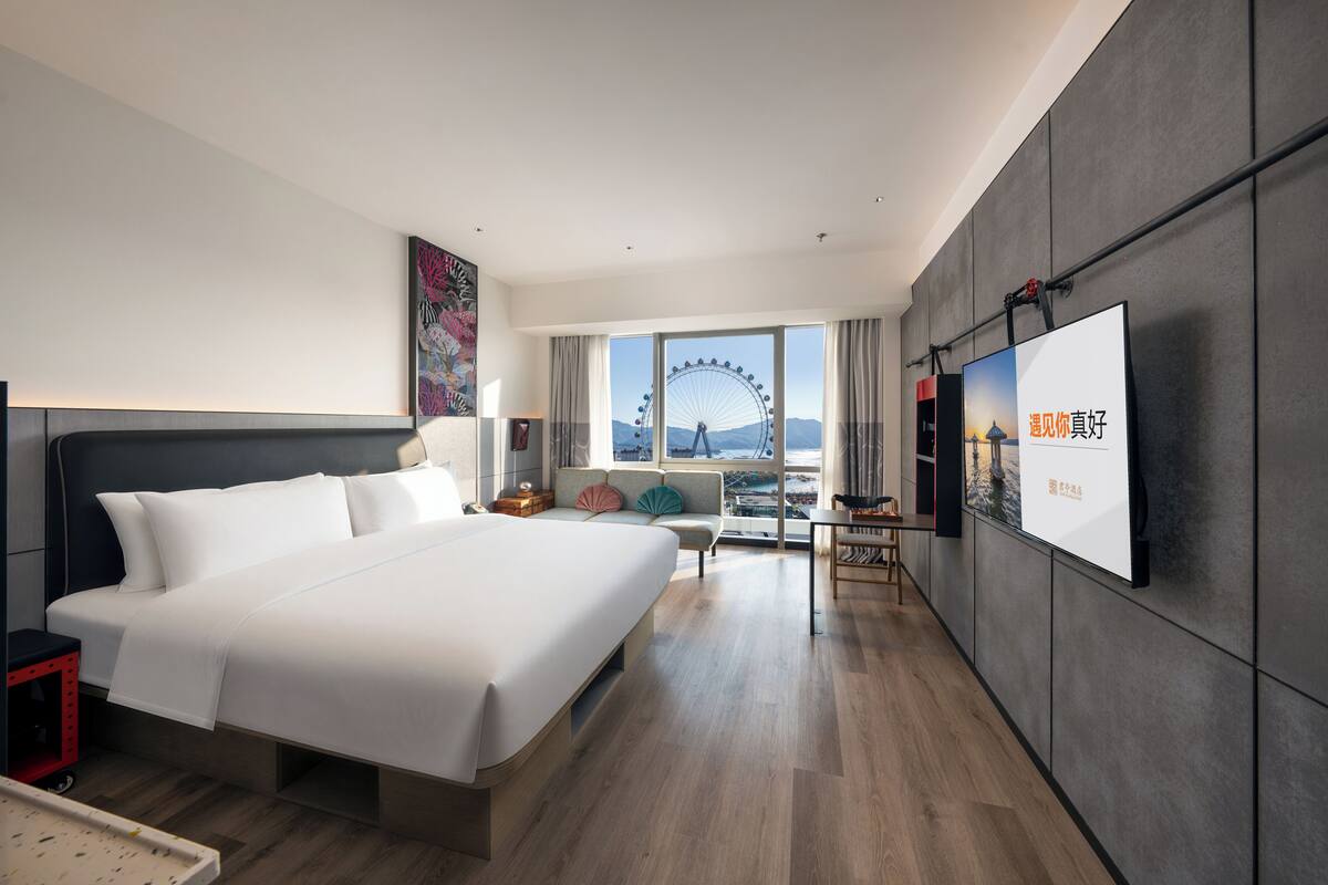 Una habitación de hotel moderna con una cama grande, un escritorio, una silla y un televisor en la pared.