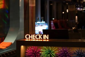 En receptionsdisk med en neonupplyst skylt som visar ”INCHECKNING”, ett fönster med utsikt över stadsbilden och en bardisk med en neonupplyst skylt.