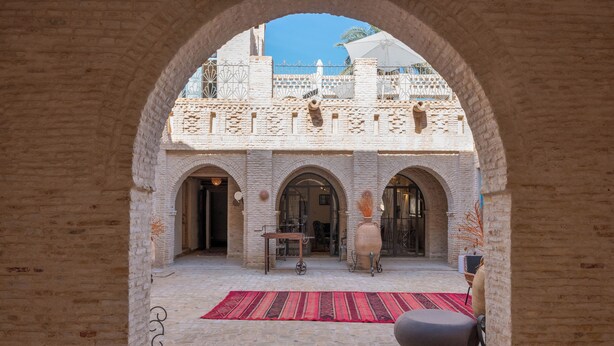 Un patio arqueado con alfombra estampada, un jarrón grande y una silla moderna.