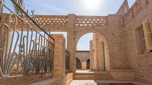 Un patio arqueado con paredes de ladrillo y portones metálicos, que conduce a un edificio con piso de baldosas.