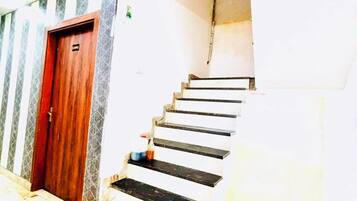 Una escalera que sube a un piso superior, una puerta de madera y un suelo de baldosas.