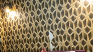 Une chambre d’hôtel avec un mur orné de motifs, un lit avec une literie blanche et rouge, et un coussin décoratif.
