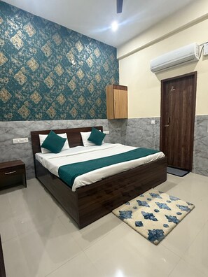 Ein Schlafzimmer mit Bett, Holz-Kopfteil, Nachttisch, Kleiderschrank, einer Tür und einem gemusterten Teppich.