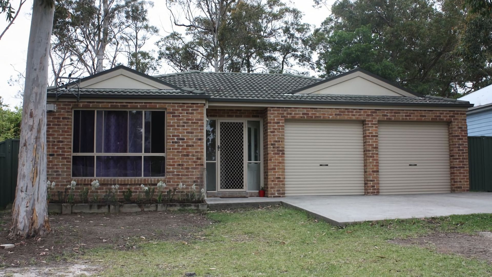 A residential building with a brick facade, a garage with two doors, and a small front yard.