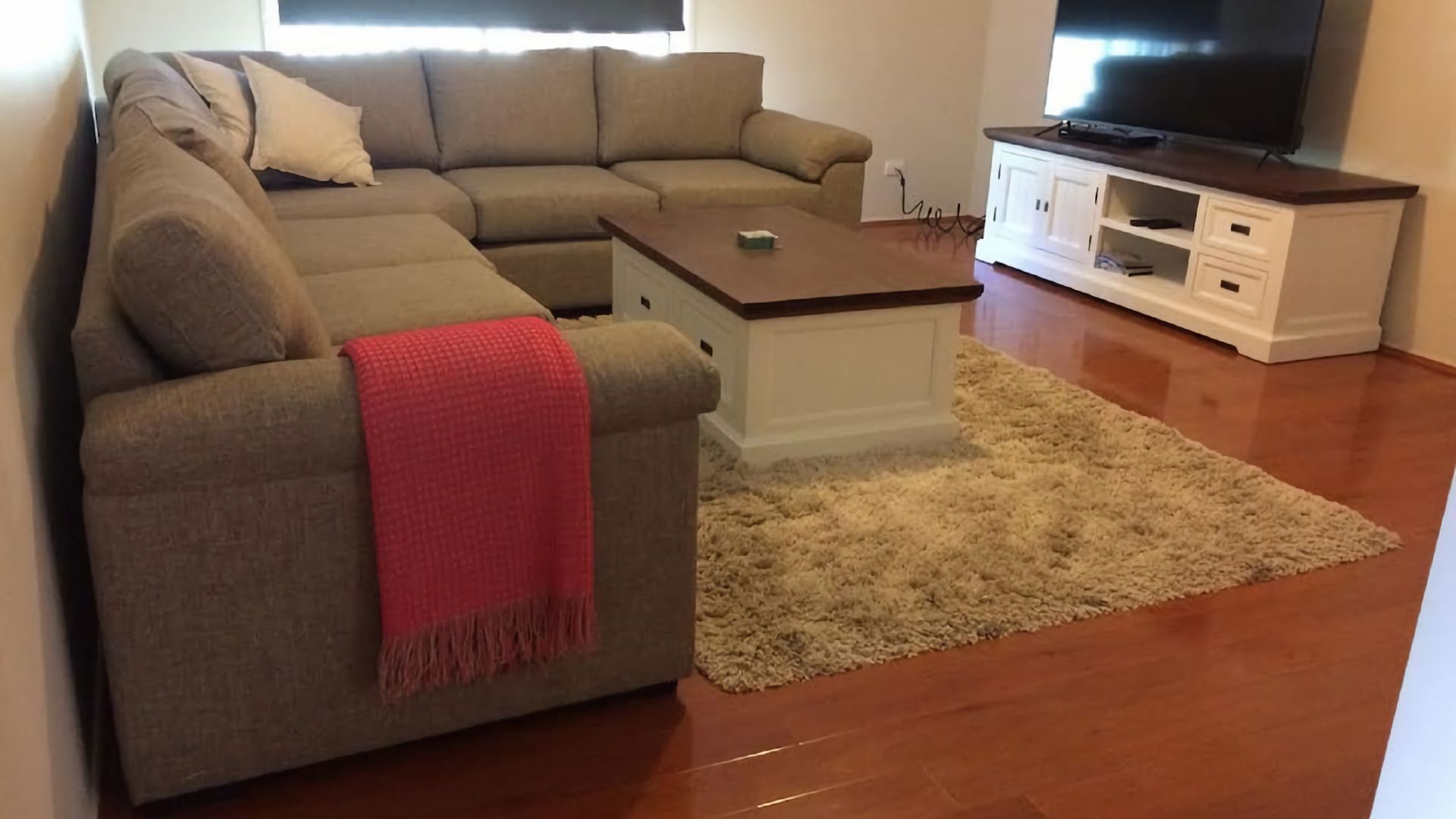 A living room with a sectional sofa, a coffee table, a TV on a stand, and a carpeted floor.