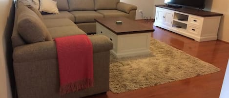 A living room with a sectional sofa, a coffee table, a TV on a stand, and a carpeted floor.