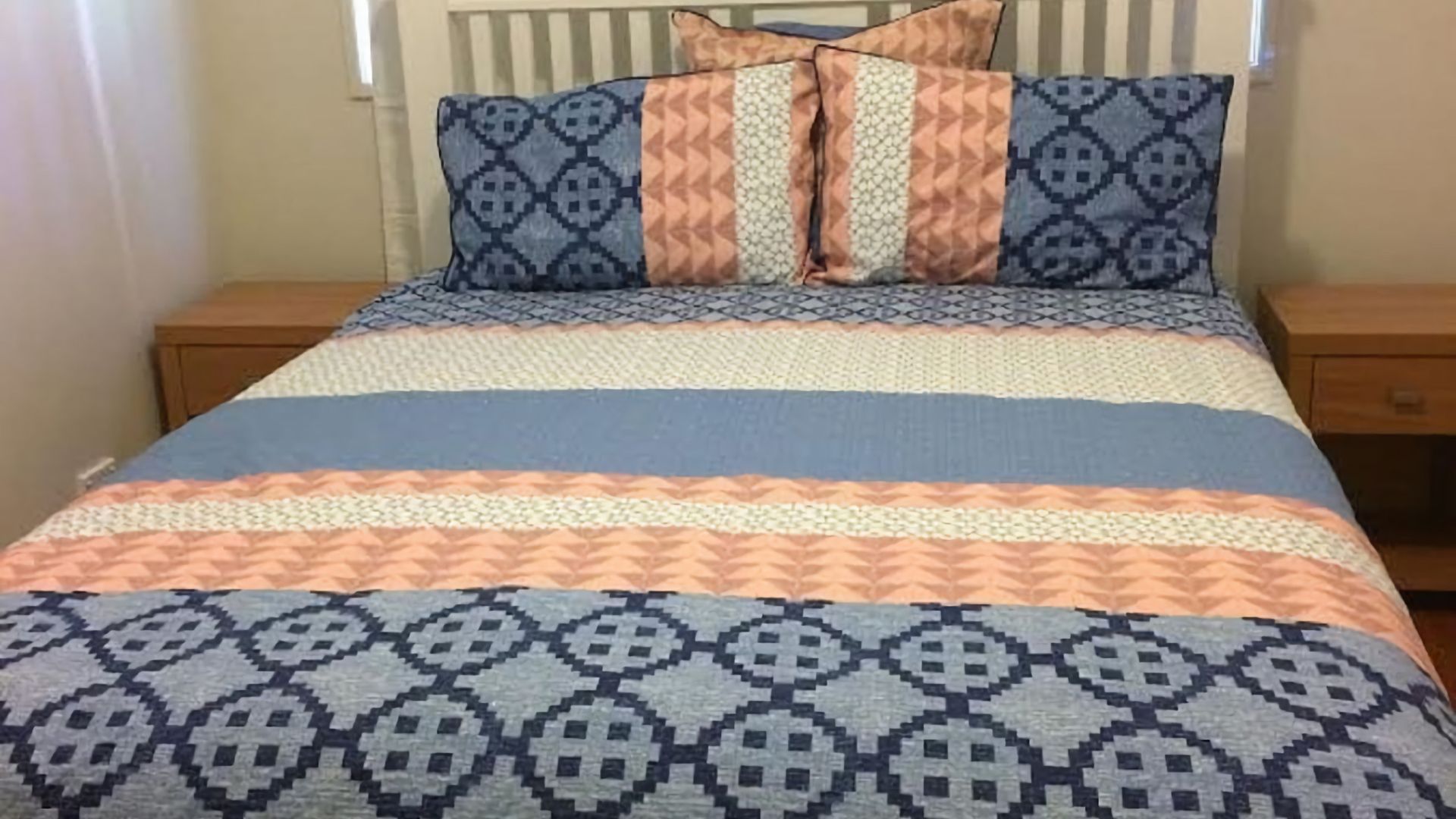 Un letto con biancheria e cuscini decorati, un comodino in legno e un mobiletto con cassetti.