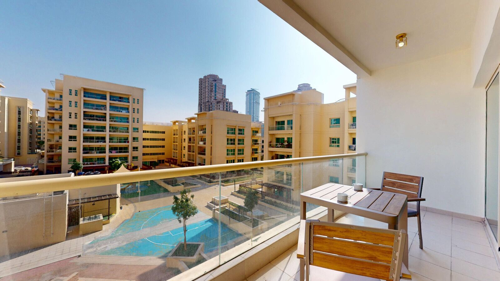 Ein Balkon mit Tisch und Stühlen, mit Blick auf einen Swimmingpool und die umliegenden Gebäude.