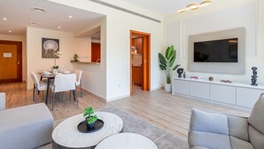 Ein modernes Wohnzimmer mit einem Flachbildfernseher, einer Essecke mit Tisch und Stühlen und einer durch eine offene Tür einsehbaren Küche.