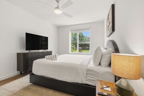 Une chambre à coucher avec un lit, une télévision, une lampe, une fenêtre et un ventilateur de plafond.