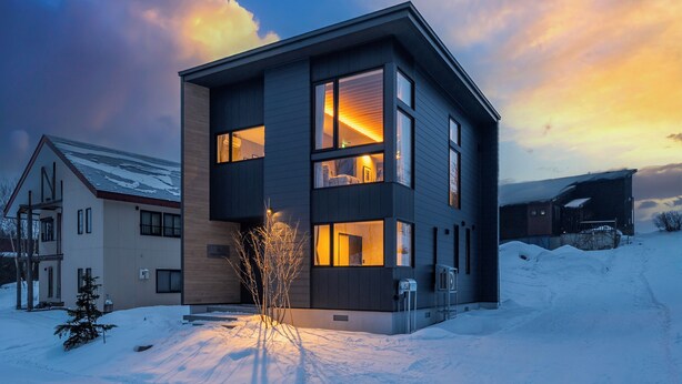 A modern two-story house with large windows, a snow-covered yard, and a sunset sky. - FURANO ECLAT (Furano)