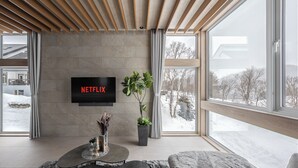 A modern living room with a large window, a flat-screen TV mounted on the wall, and a potted plant. - FURANO ECLAT (Furano)