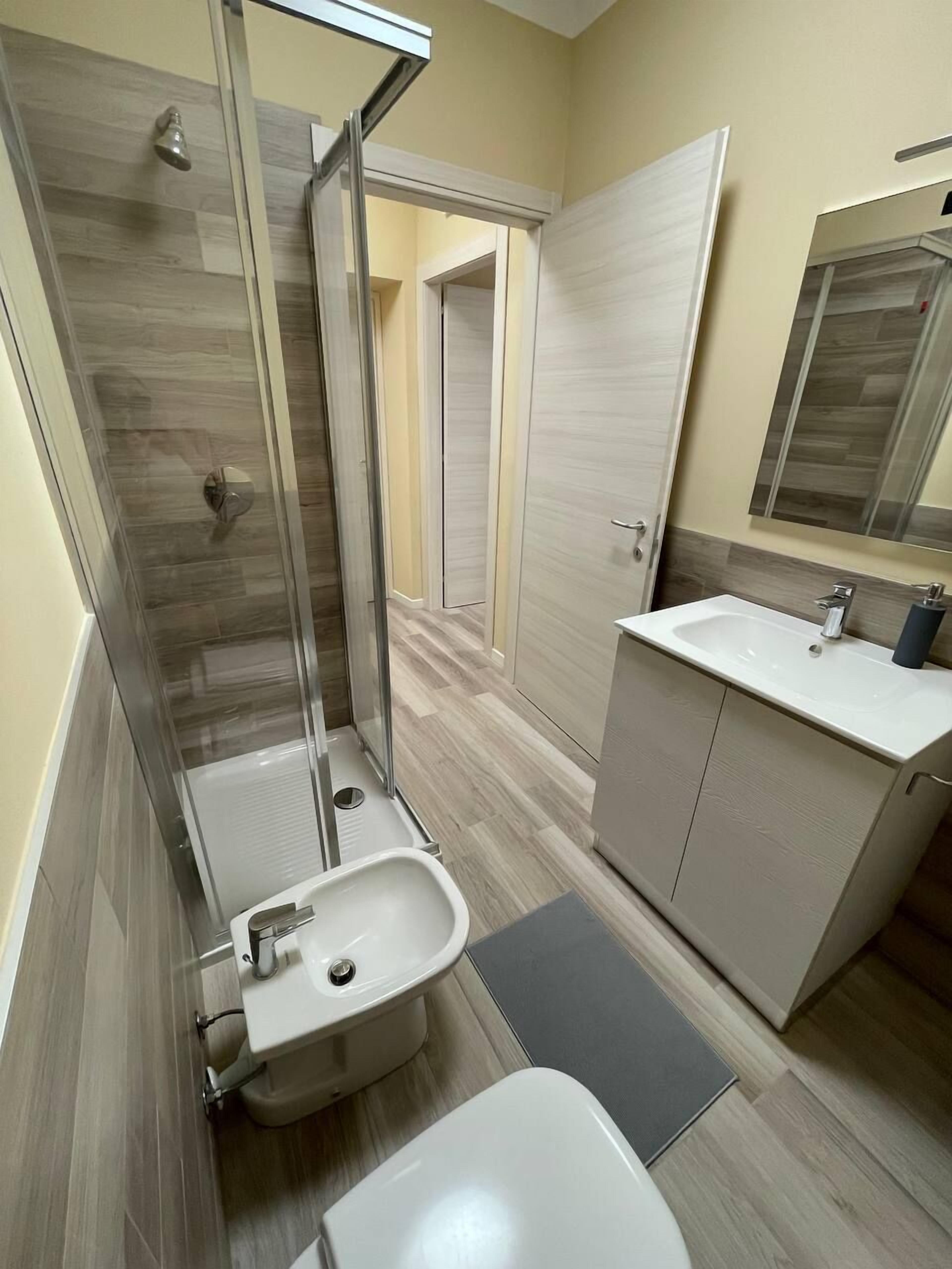 Un baño moderno con cabina de ducha de vidrio, lavamanos pedestal y tocador con espejo.