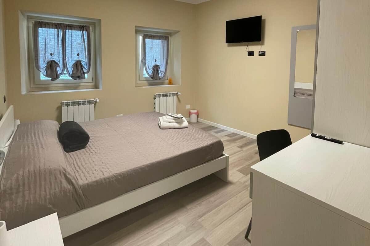 Une chambre moderne avec un lit, un bureau, une télévision et deux fenêtres équipées de rideaux.