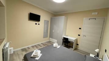 Una habitación de hotel con cama, escritorio, armario y televisor.
