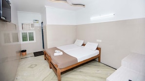 Ein Schlafzimmer mit einem Einzelbett, einem Deckenventilator, einem flachbildfernseher an der Wand und einem Fenster mit Klimaanlagen.