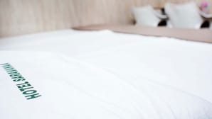 Ein Hotelbett mit einem Kopfkissen, auf dem der Schriftzug „HOTEL SHANGHAI“ zu sehen ist.