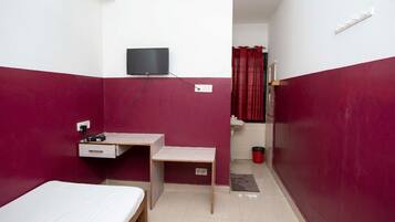 A small, compact room with a bed, a desk, and a television.