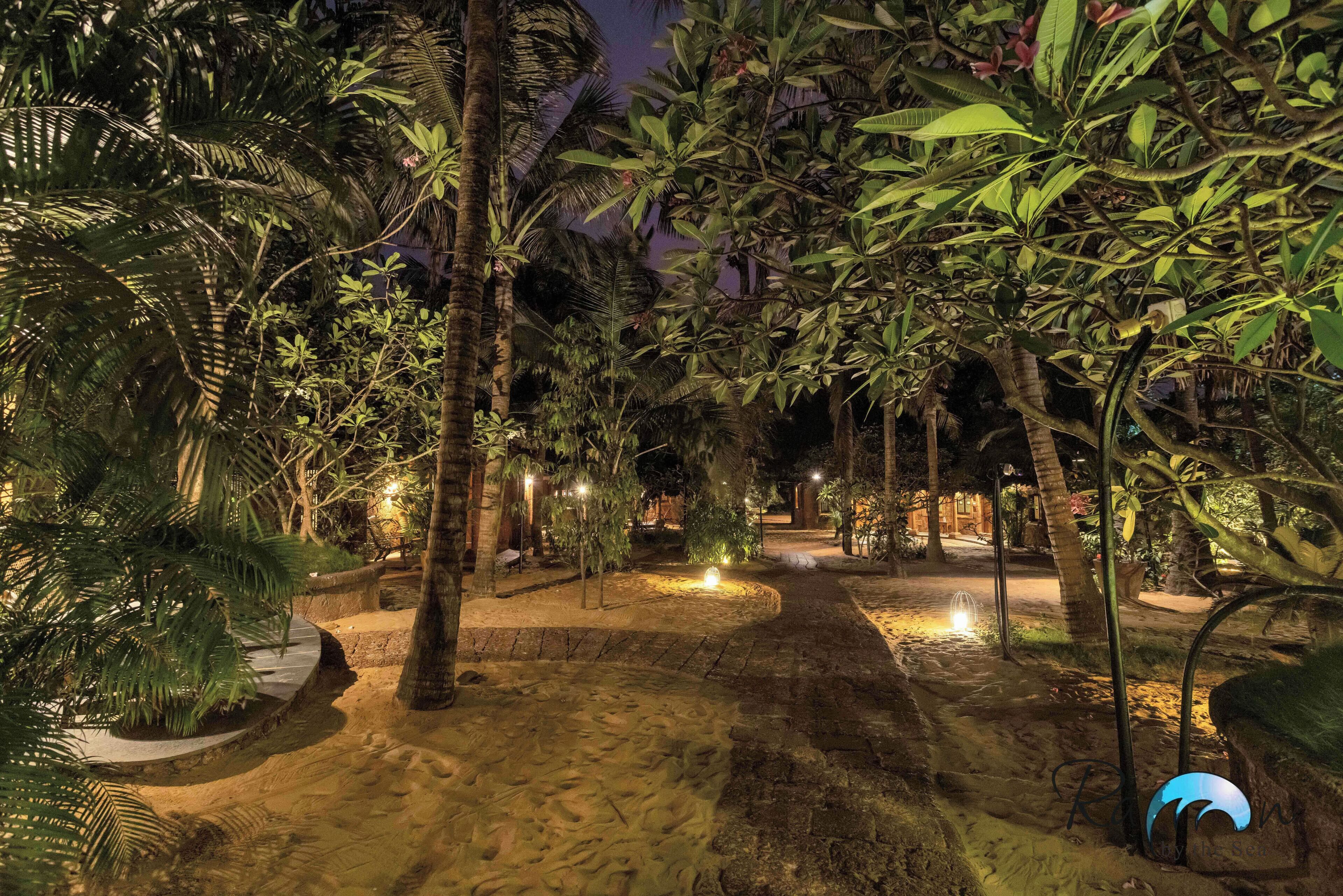 A nighttime garden with pathways, palm trees, and ambient lighting.