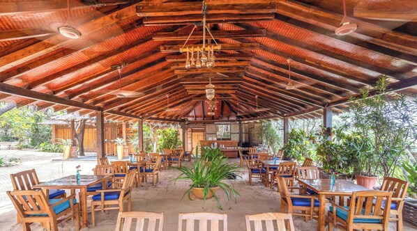 A covered outdoor dining area with wooden tables and chairs, potted plants, and a rustic wooden ceiling. - Raman Resort (Calangute)