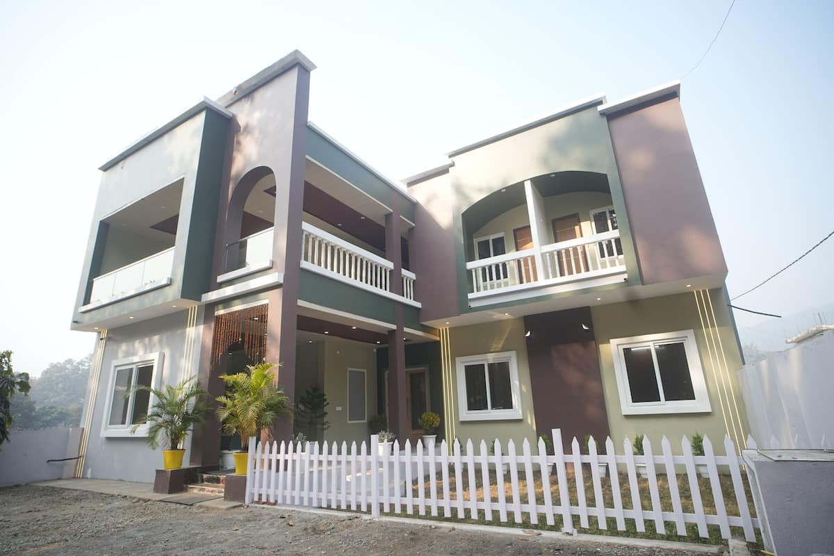 A two-story residential building with balconies, a white picket fence, and potted plants.