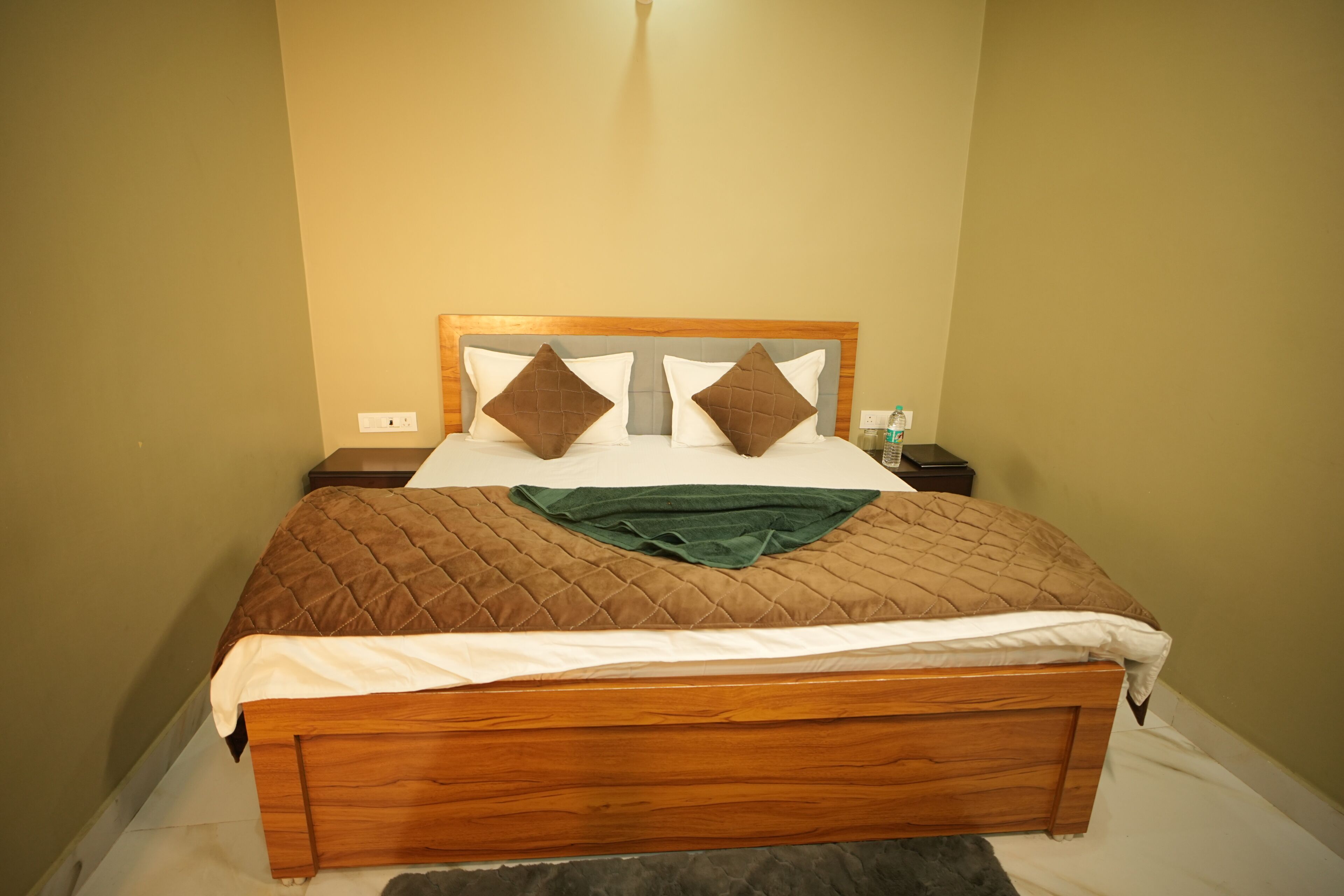 Ein ordentlich bezogenes Bett mit Holzbettgestell, einer braunen Bettdecke, zwei Kissen und einer grünen Decke.