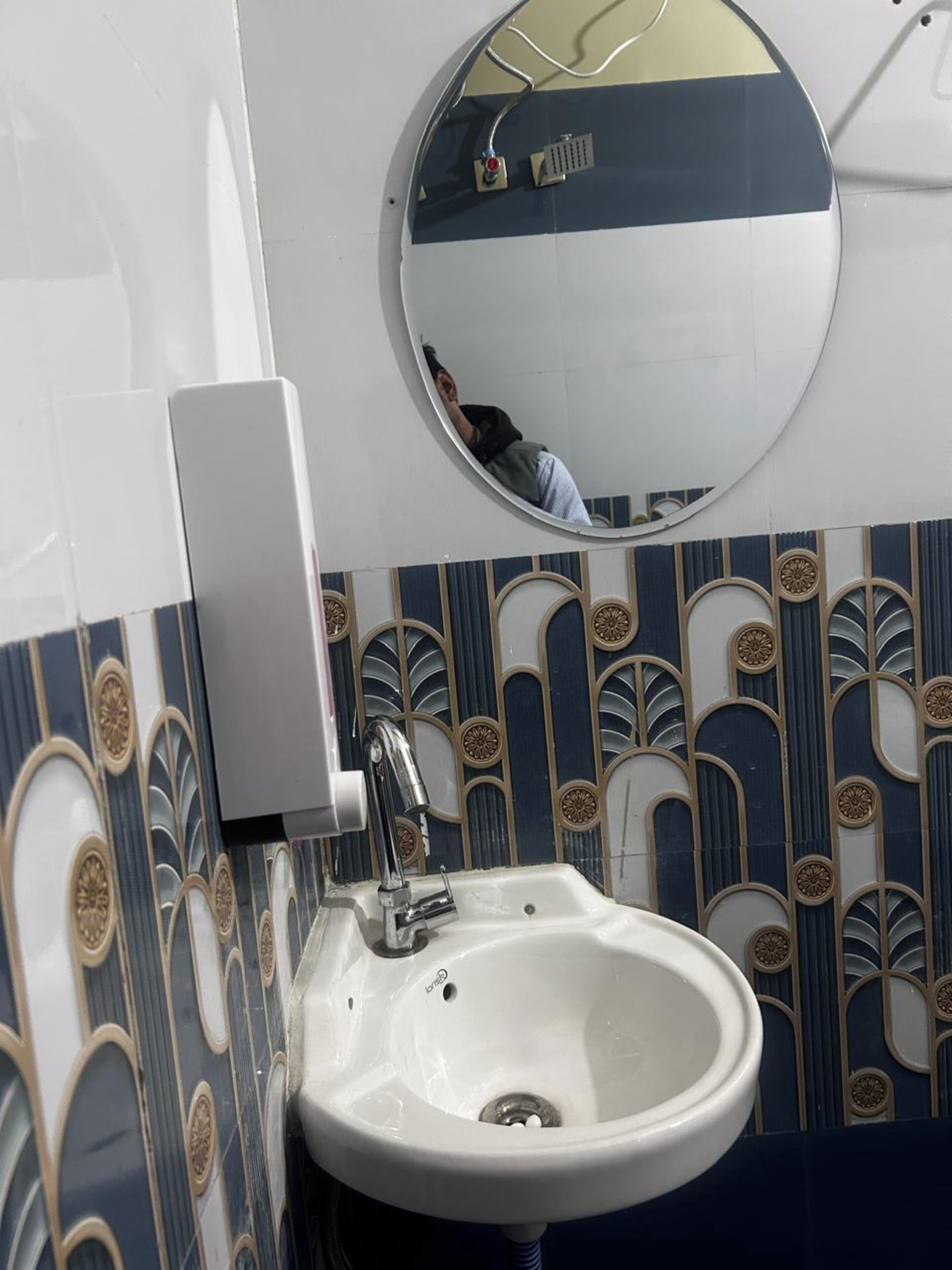 A bathroom with a white sink, a mirror, and decorative wall tiles.