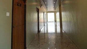A hallway with a wooden door, a marble floor, and a ceiling with recessed lighting. - GREEN VALLEY HOTEL AND RESORT (Haldwani)