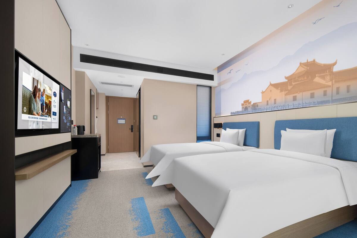 Habitación de hotel con dos camas, un televisor, un escritorio y un mural de arquitectura tradicional.