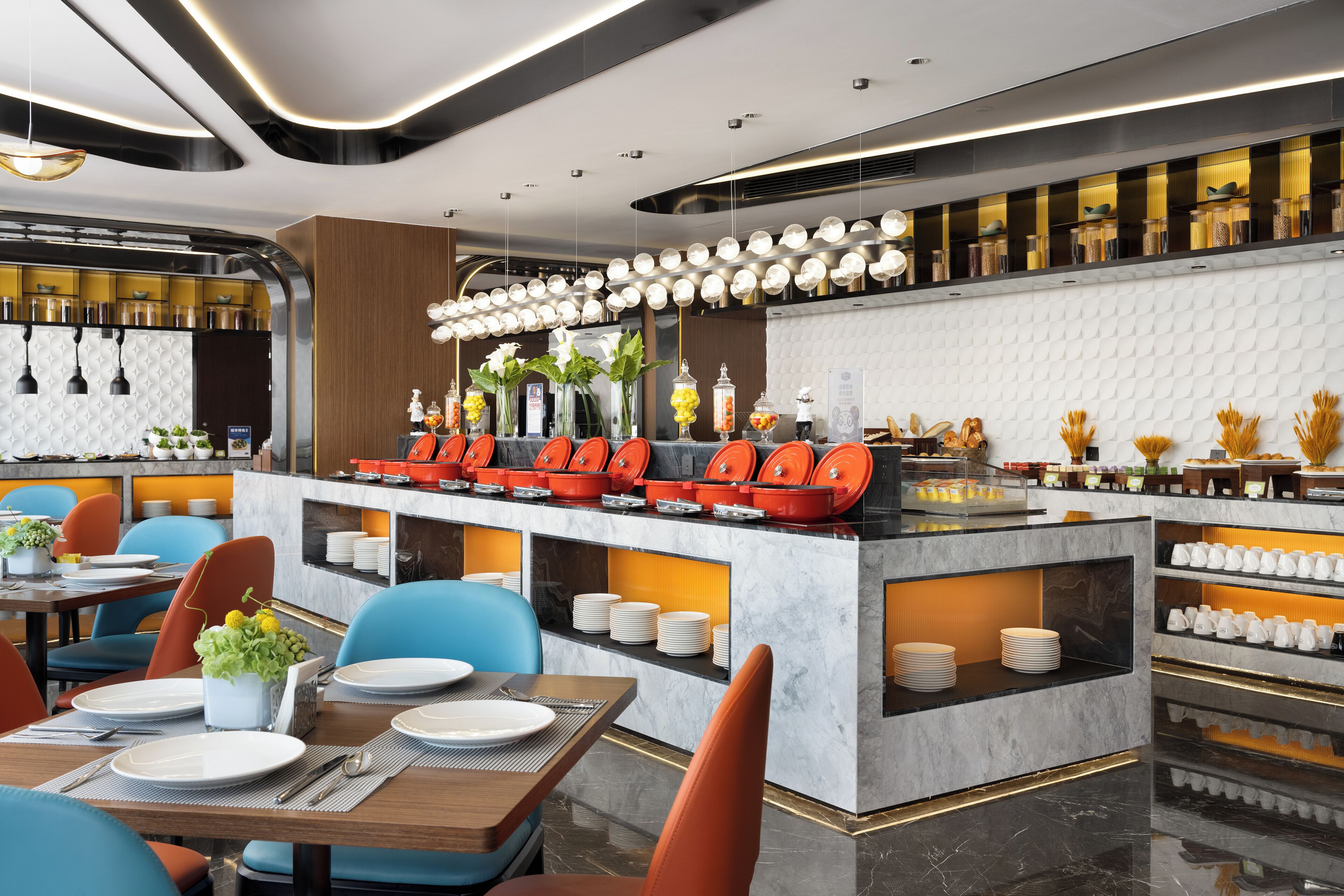 A modern restaurant with a central island, blue and orange chairs, and a variety of dishes displayed on shelves.