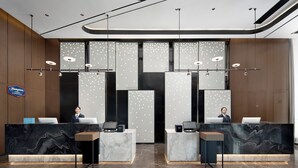 Un hall d’accueil moderne avec des comptoirs de réception en marbre, un grand écran numérique et une enseigne indiquant « Hampton Inn ».