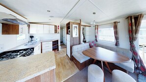 Interior compacto de una casa rodante con kitchenette, comedor y asientos.