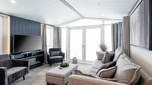Een moderne woonkamer met een flatscreen televisie, comfortabele zitplaatsen en een groot raam.