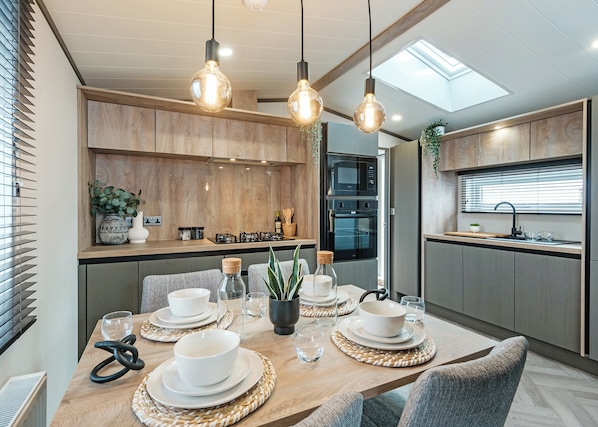 A modern kitchen with wooden cabinets, a built-in oven, and a dining area with a table set for four.