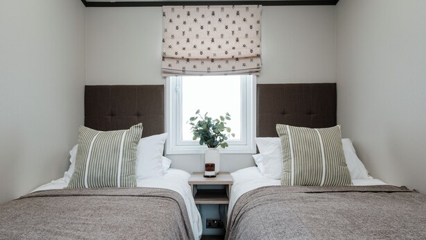 Een tweepersoonskamer met twee bedden, een raam met een plant en een nachtkastje met een lamp.