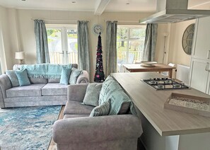 A cozy living room with a sofa, armchair, and a small kitchen area with a gas stove. - 2 bedroom accommodation in Cartmel (Cartmel)